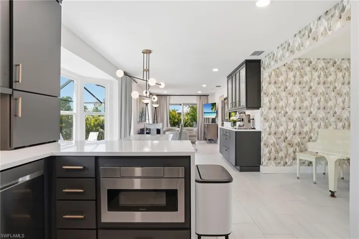 Kitchen with a peninsula, open floor plan, light stone counters, a chandelier, and wallpapered walls - Virtually Edited Image
