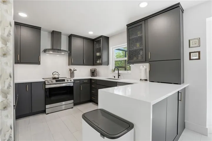 Kitchen with glass insert cabinets, a peninsula, stainless steel range with electric stovetop, recessed lighting, and light stone counters - Virtually Edited Image