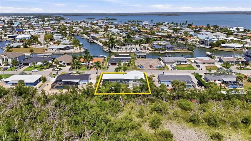 Aerial view of residential area featuring property parcel outlined and a nearby body of water - Virtually Edited Image