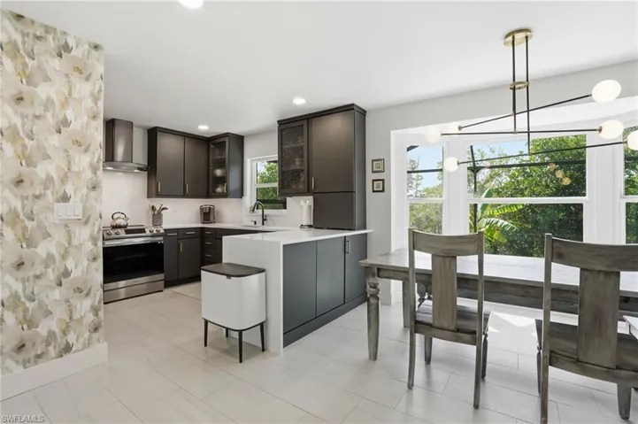 Kitchen with glass insert cabinets, a peninsula, stainless steel electric stove, a kitchen bar, and pendant lighting - Virtually Edited Image