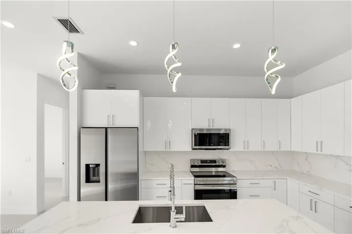 Kitchen featuring hanging light fixtures, appliances with stainless steel finishes, light stone counters, modern cabinets, and white cabinets