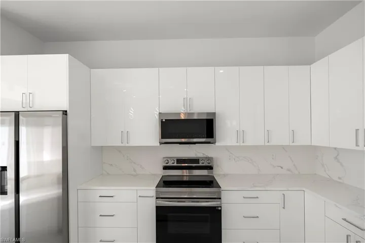 Kitchen with appliances with stainless steel finishes, white cabinets, modern cabinets, and light stone counters