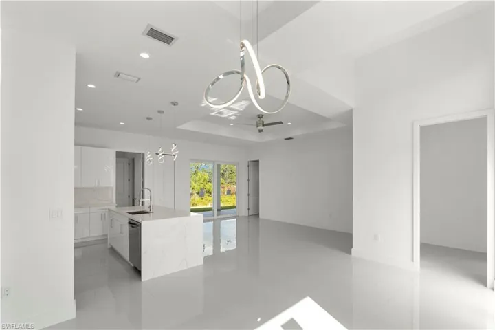 Kitchen featuring white cabinetry, a chandelier, a tray ceiling, hanging light fixtures, and light stone counters