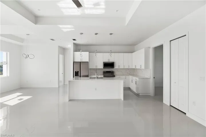 Kitchen with white cabinetry, hanging light fixtures, stainless steel appliances, a center island with sink, and a tray ceiling