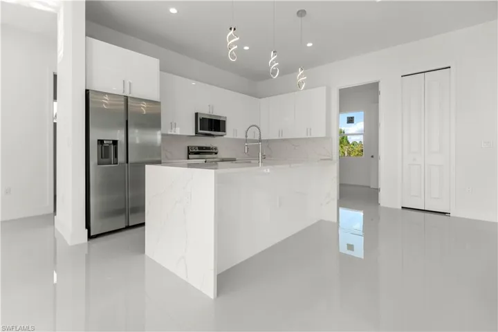 Kitchen with appliances with stainless steel finishes, white cabinetry, light stone countertops, decorative light fixtures, and recessed lighting