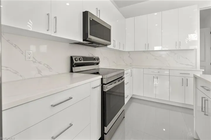Kitchen featuring stainless steel appliances, backsplash, modern cabinets, white cabinetry, and light stone countertops