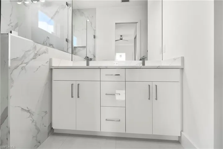 Bathroom featuring double vanity, a marble finish shower, and a ceiling fan