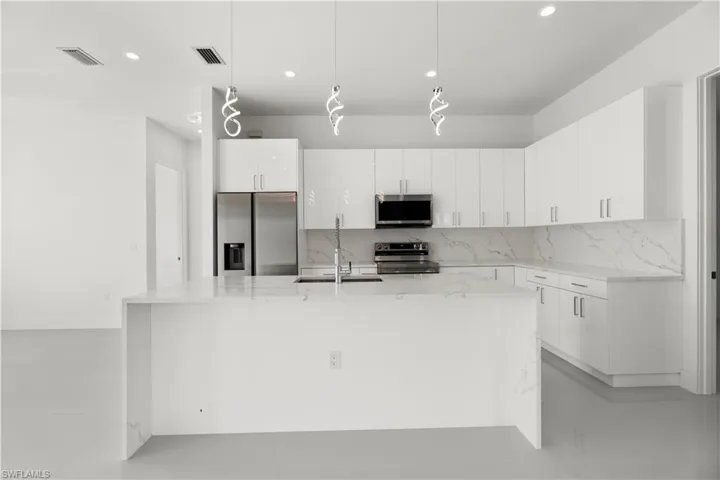 Kitchen featuring light stone countertops, hanging light fixtures, stainless steel appliances, tasteful backsplash, and white cabinetry