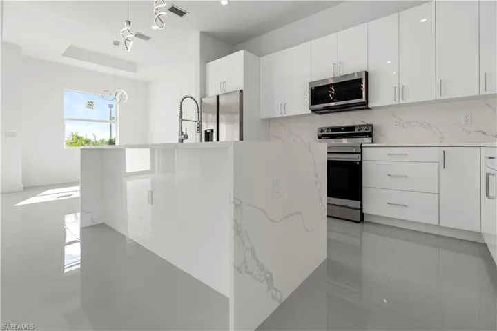 Kitchen featuring appliances with stainless steel finishes, light stone counters, modern cabinets, and white cabinets