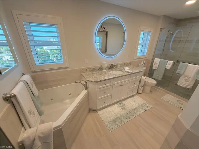 Full bath with vanity, a shower stall, a tub with jets, and light wood-type flooring