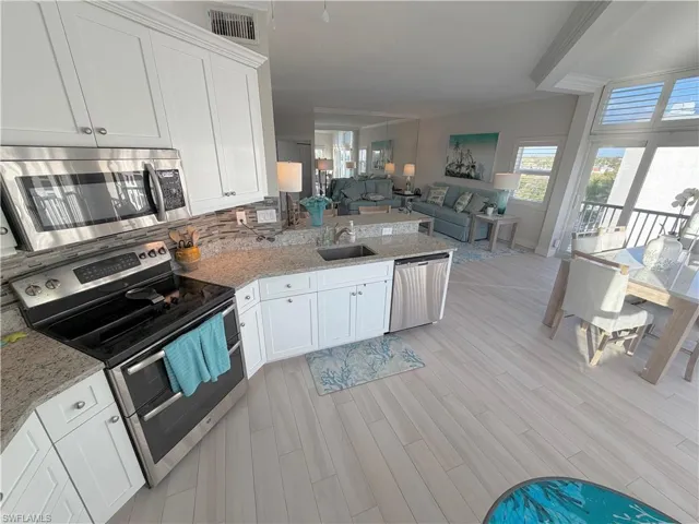 Kitchen with stainless steel appliances, light stone counters, ornamental molding, a peninsula, and white cabinetry