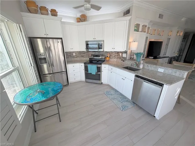 Kitchen with appliances with stainless steel finishes, white cabinets, ornamental molding, light stone countertops, and a peninsula