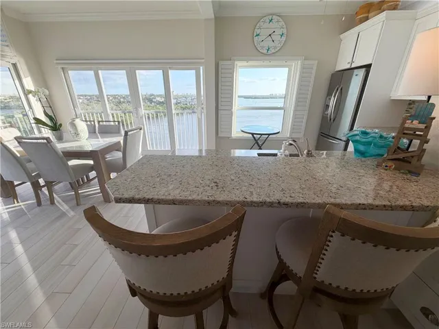 Kitchen featuring light stone counters, a peninsula, white cabinetry, a water view, and stainless steel refrigerator with ice dispenser