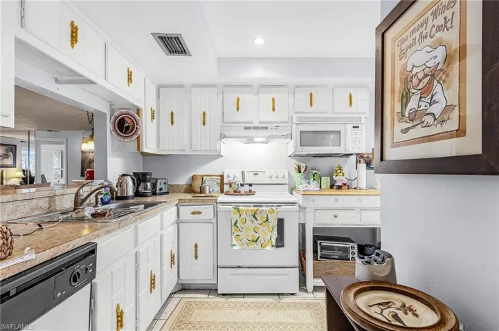 Kitchen featuring white cabinets, white appliances, light countertops, under cabinet range hood, and recessed lighting