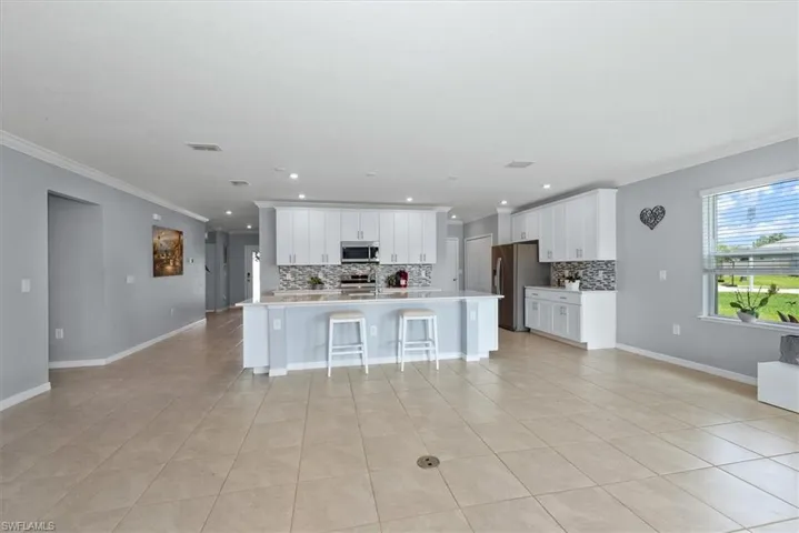 Kitchen featuring appliances with stainless steel finishes, crown molding, decorative backsplash, light tile patterned floors, and a kitchen breakfast bar