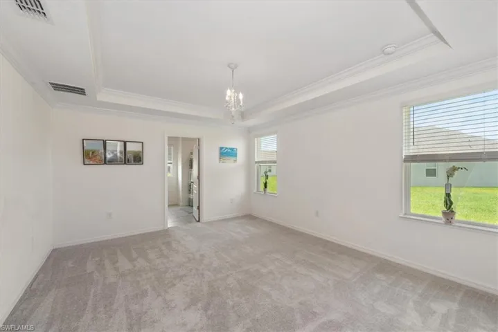 Spare room featuring a tray ceiling, crown molding, a chandelier, light carpet, and a smoke detector