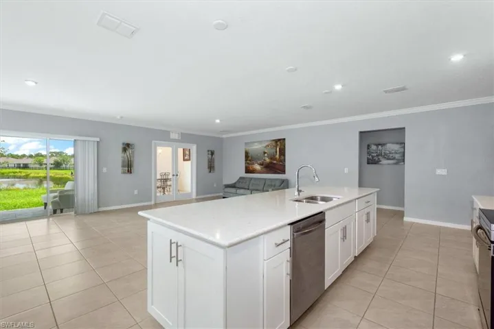 Kitchen with dishwasher, open floor plan, light tile patterned floors, crown molding, and a center island with sink