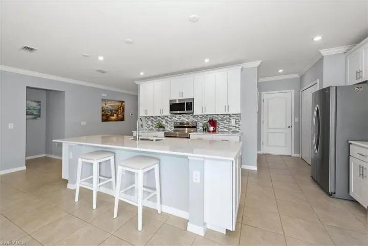 Kitchen with stainless steel appliances, ornamental molding, light tile patterned floors, decorative backsplash, and a kitchen island with sink