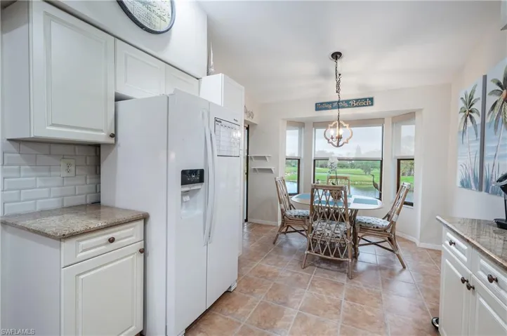 Kitchen with white cabinetry, light stone counters, white refrigerator with ice dispenser, decorative light fixtures, and decorative backsplash