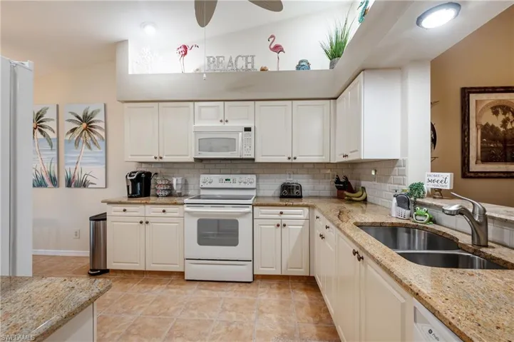 Kitchen featuring lofted ceiling, backsplash, white appliances, sink, and white cabinetry