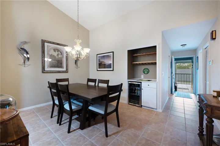 Tiled dining room featuring bar area, high vaulted ceiling, beverage cooler, and a notable chandelier