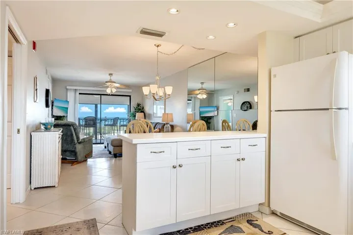 Kitchen with open floor plan, freestanding refrigerator, white cabinets, suspended lighting, and ceiling fan