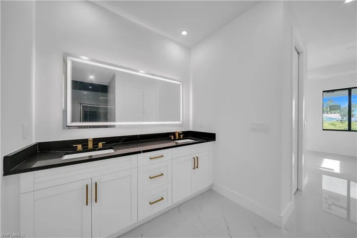 Full bath with double vanity, a shower stall, light marble finish floors, and recessed lighting