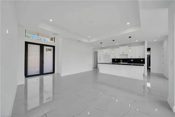 Unfurnished living room with a raised ceiling, light marble finish flooring, recessed lighting, and french doors