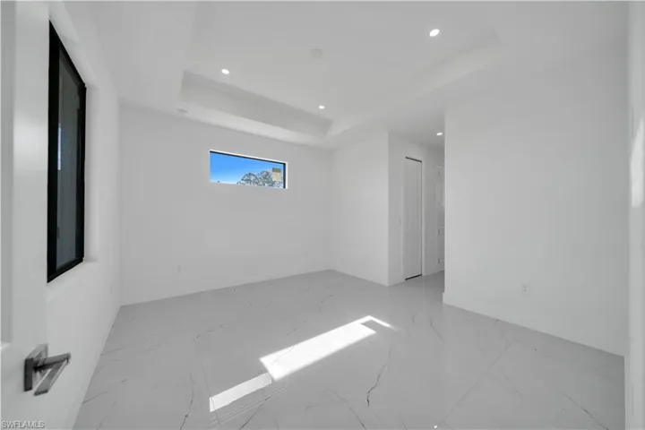 Empty room with light marble finish flooring, a tray ceiling, and recessed lighting