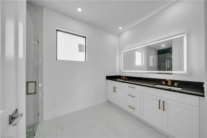 Bathroom with a marble finish shower, double vanity, light marble finish flooring, and recessed lighting