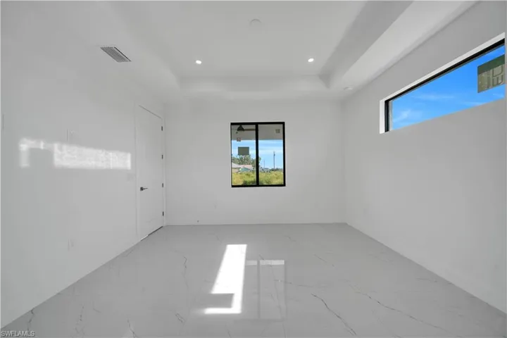 Spare room featuring light marble finish floors, a raised ceiling, and recessed lighting
