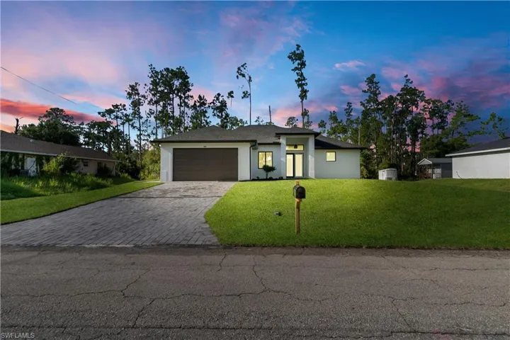 View of front facade featuring a front yard, decorative driveway, a garage, and stucco siding