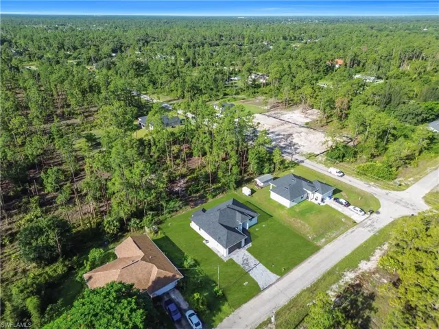 Aerial view of property and surrounding area featuring nearby suburban area and a heavily wooded area
