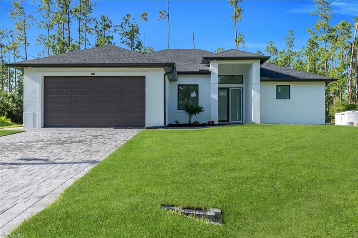 View of front of house featuring roof with shingles, a front lawn, decorative driveway, and stucco siding