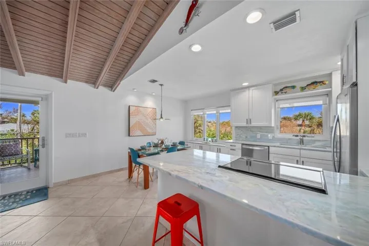 Kitchen with lofted ceiling with beams, light stone counters, stainless steel appliances, pendant lighting, and white cabinets