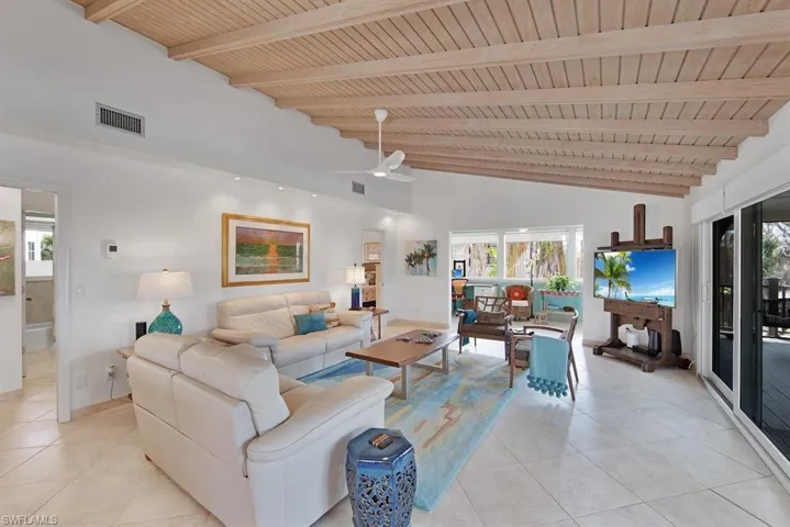 Living room with wooden ceiling, light tile patterned flooring, beamed ceiling, ceiling fan, and high vaulted ceiling