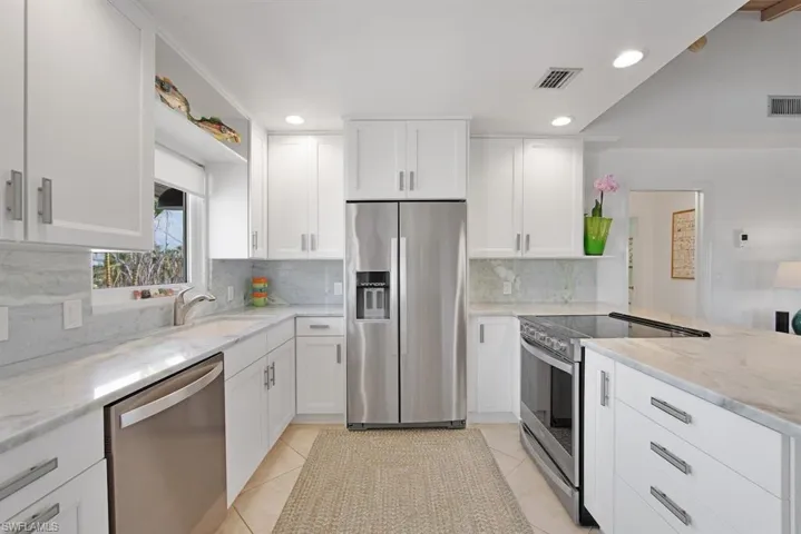 Kitchen with white cabinetry, decorative backsplash, stainless steel appliances, and light tile patterned floors