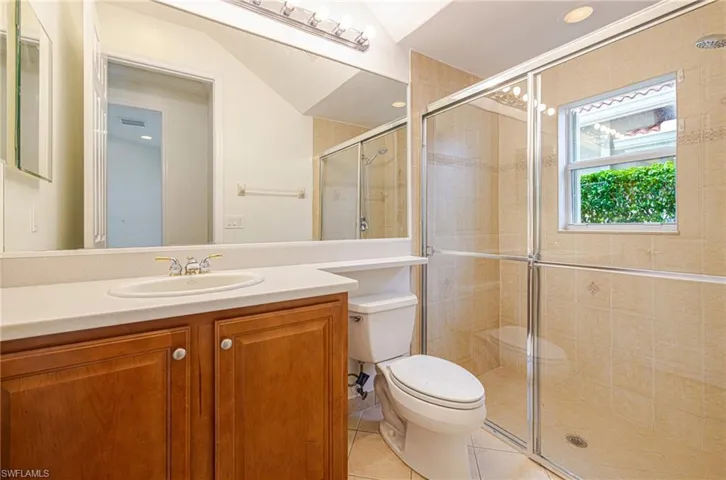 Bathroom featuring a wood-finish vanity, light-toned countertop with an integrated sink, and a glass-enclosed shower with tiled walls
