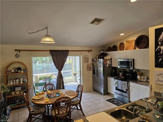 Kitchen featuring stainless steel appliances, vaulted ceiling, white cabinets, light tile patterned floors, and dark countertops