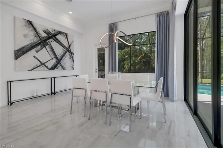 Dining room overlooking the treed yard through a picture window with plenty of natural light, porcelain tile floors, and a decorative chandelier