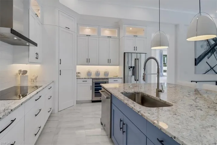 Kitchen with stainless steel JennAir appliances, granite counters, oversized island with sink, upscale white cabinetry, a 12' ceilings, and a second course of upper glass-door cabinets and cabinet pantry door