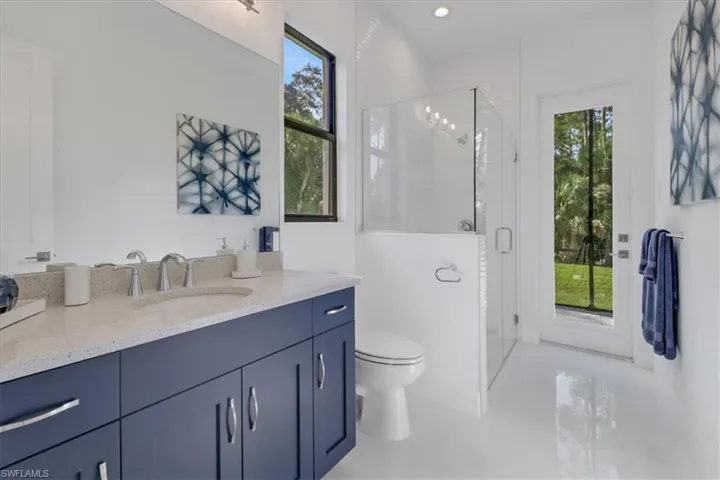 Bathroom featuring a shower with decorative tile and frameless glass doors, Quartz vanity, and high-gloss tile floors