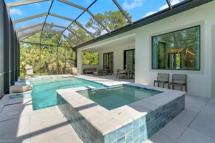 View of swimming pool featuring a porcelain tile decking, a salt-water pool with sunshelf, spillover bowls, and a spa with a large covered lanai featuring ceiling fans and recessed lighting