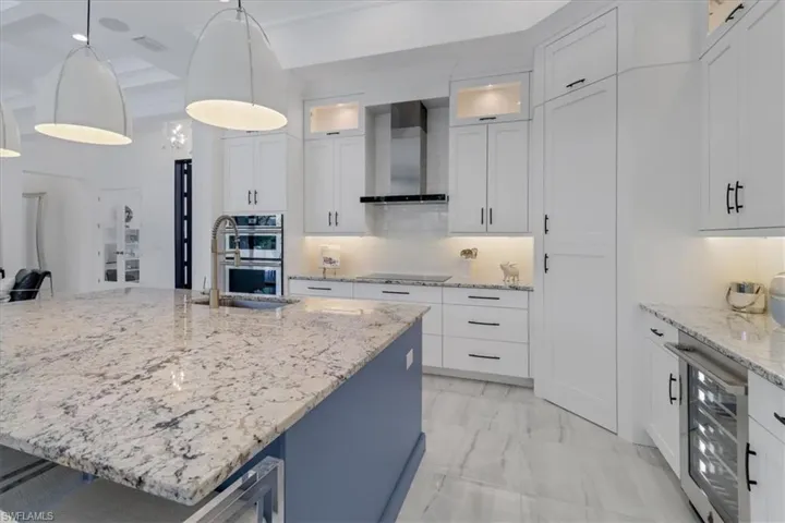 Kitchen with stainless steel JennAir appliances, granite counters, oversized island with sink, upscale white cabinetry, a 12' ceilings, and a second course of upper glass-door cabinets and cabinet pantry door