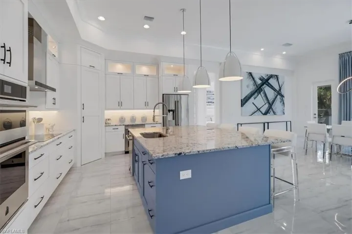 Kitchen with stainless steel JennAir appliances, granite counters, oversized island with sink, upscale white cabinetry, a 12' ceilings, and a second course of upper glass-door cabinets and cabinet pantry door