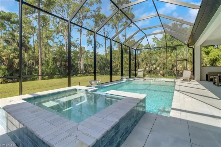 View of pool with screen cage overlooking the heavily treed backyard