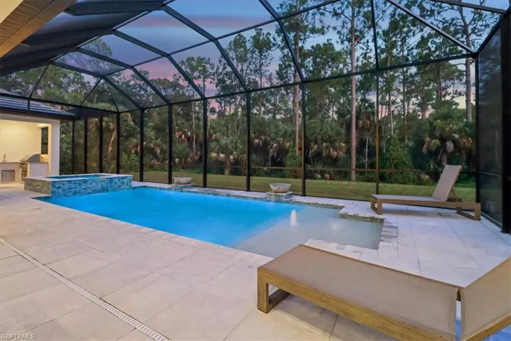 Pool at dusk featuring a patio, a pool with connected hot tub, and glass enclosure
