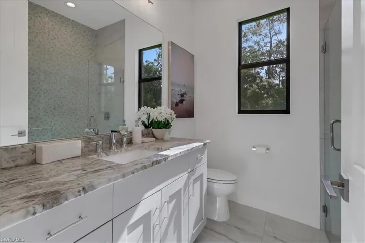 Full bathroom granite vanity and stand-up shower with frameless glass doors and decorative tile surrounds