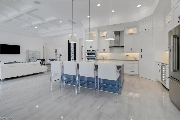 Kitchen with stainless steel JennAir appliances, granite counters, oversized island with sink, upscale white cabinetry, a 12' ceilings, and a second course of upper glass-door cabinets and cabinet pantry door