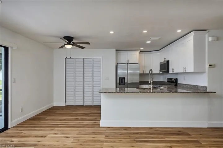 Kitchen featuring stainless steel appliances, dark stone counters, a peninsula, white cabinets, and light wood-style floors